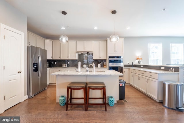 kitchen featuring tasteful backsplash, a sink, appliances with stainless steel finishes, an island with sink, and wood finished floors