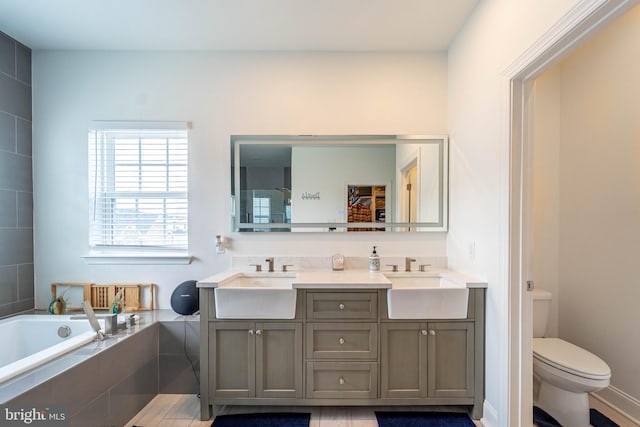full bath featuring toilet, a bath, double vanity, and a sink