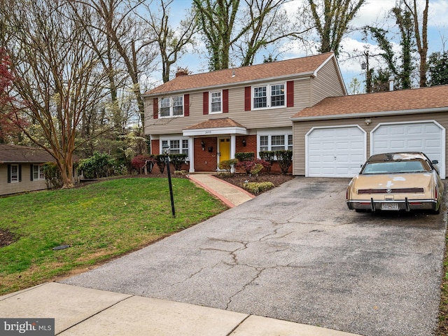 colonial-style house with a front yard, an attached garage, a chimney, brick siding, and driveway