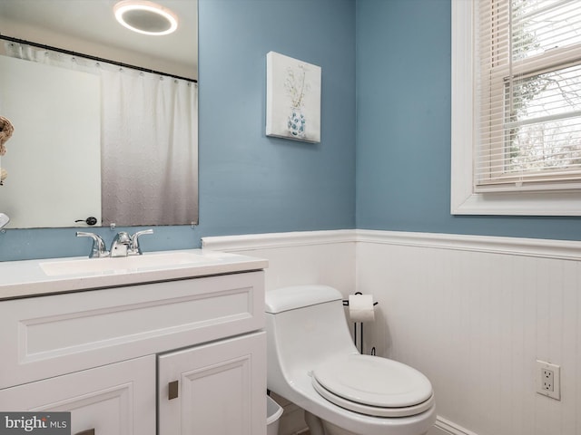 bathroom with toilet, vanity, and a wainscoted wall