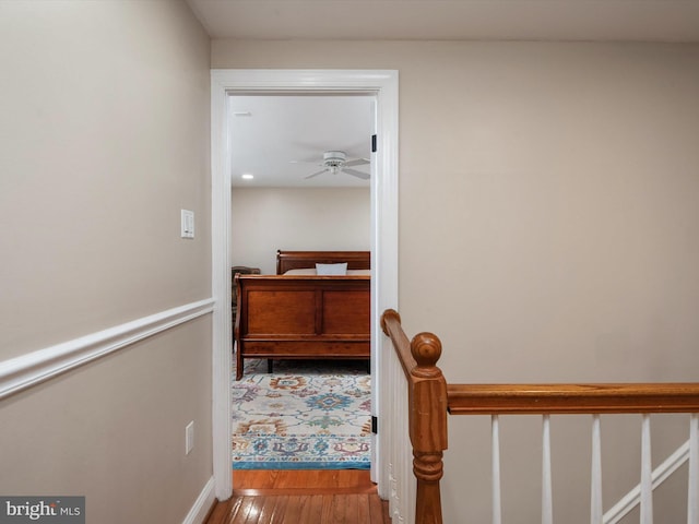 corridor with baseboards, an upstairs landing, and wood finished floors