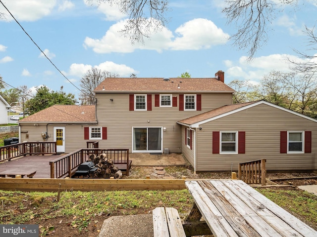 rear view of house with roof with shingles, a chimney, and a wooden deck
