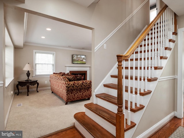 staircase featuring baseboards, ornamental molding, a fireplace, carpet flooring, and visible vents