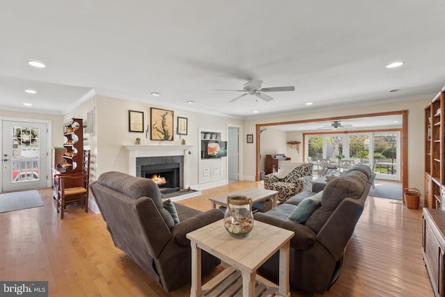 living room featuring a wealth of natural light, a ceiling fan, a tile fireplace, and light wood-style floors