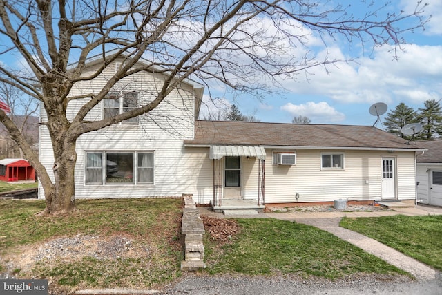 view of front facade with a front lawn, an AC wall unit, and roof with shingles