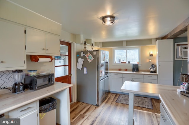 kitchen featuring light countertops, freestanding refrigerator, black microwave, light wood finished floors, and white cabinetry