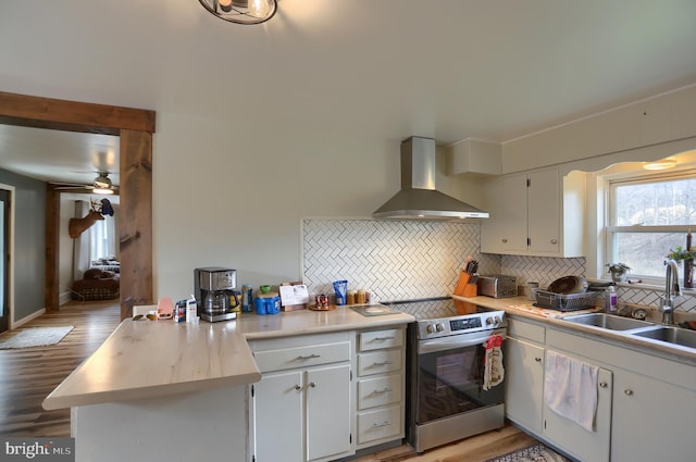 kitchen with light countertops, backsplash, a sink, wall chimney range hood, and electric range