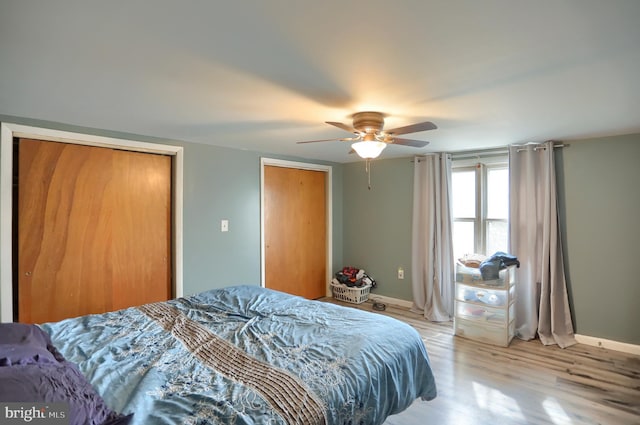 bedroom with two closets, baseboards, light wood finished floors, and ceiling fan
