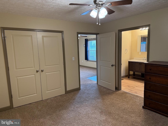 unfurnished bedroom featuring a closet, a textured ceiling, ensuite bath, baseboards, and carpet