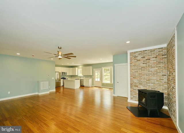 unfurnished living room with baseboards, a ceiling fan, a wood stove, visible vents, and light wood finished floors