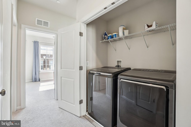 clothes washing area with washer and clothes dryer, visible vents, laundry area, and light carpet