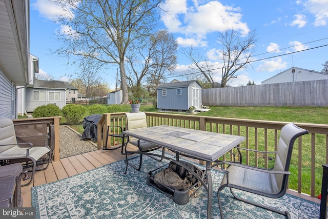wooden deck featuring outdoor dining space, a shed, an outbuilding, a yard, and fence