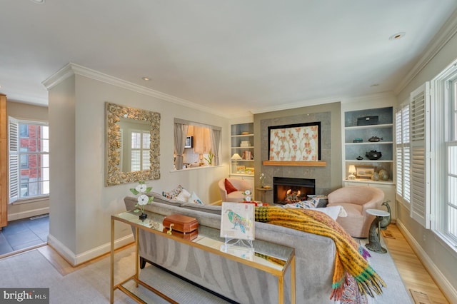 living area with crown molding, light wood-style floors, built in shelves, baseboards, and a tile fireplace