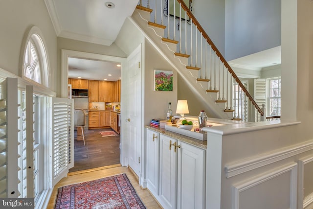 bar featuring stairway, crown molding, stainless steel microwave, and light wood-style flooring