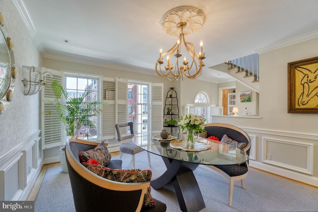dining room featuring wainscoting, stairway, a notable chandelier, ornamental molding, and a decorative wall