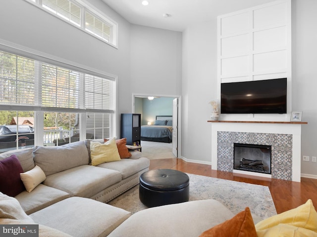 living room featuring baseboards, wood finished floors, a high ceiling, and a fireplace