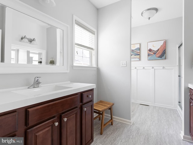 bathroom featuring wood finished floors, a shower with door, vanity, baseboards, and visible vents