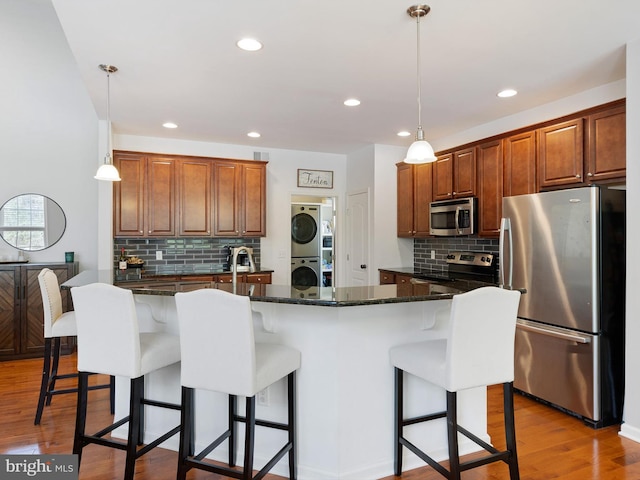 kitchen featuring stacked washer and clothes dryer, stainless steel appliances, decorative backsplash, light wood-style flooring, and a breakfast bar area