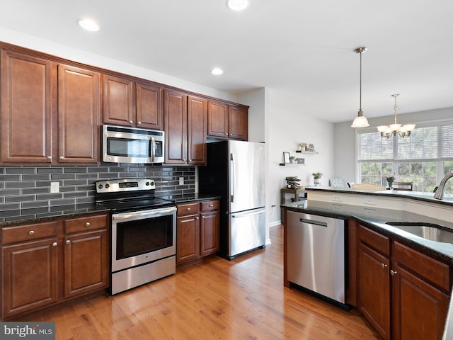kitchen with stainless steel appliances, an inviting chandelier, backsplash, dark stone countertops, and a sink