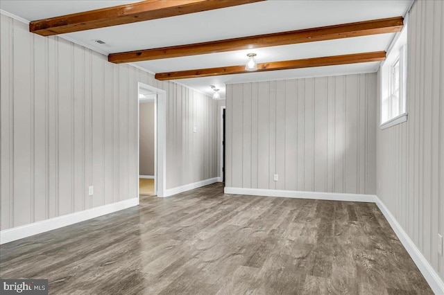 spare room featuring visible vents, beam ceiling, baseboards, and wood finished floors
