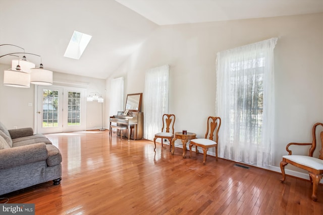 living area featuring a skylight, visible vents, high vaulted ceiling, and wood-type flooring