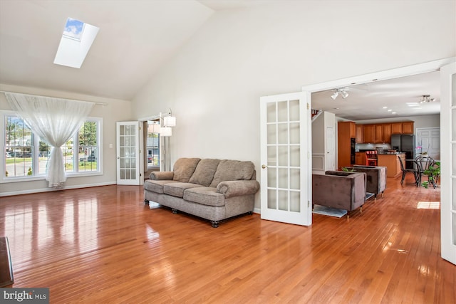 living area with light wood-type flooring, a skylight, high vaulted ceiling, and french doors