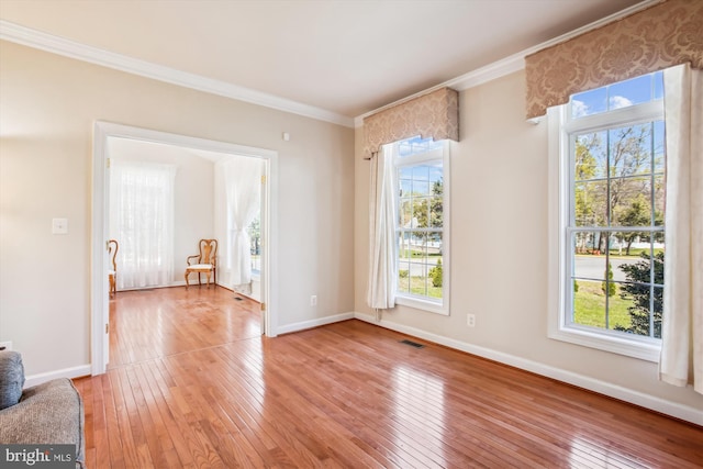 empty room featuring light wood-style flooring, visible vents, a wealth of natural light, and ornamental molding