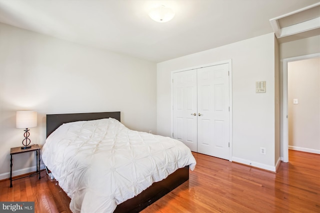 bedroom with attic access, baseboards, wood finished floors, and a closet