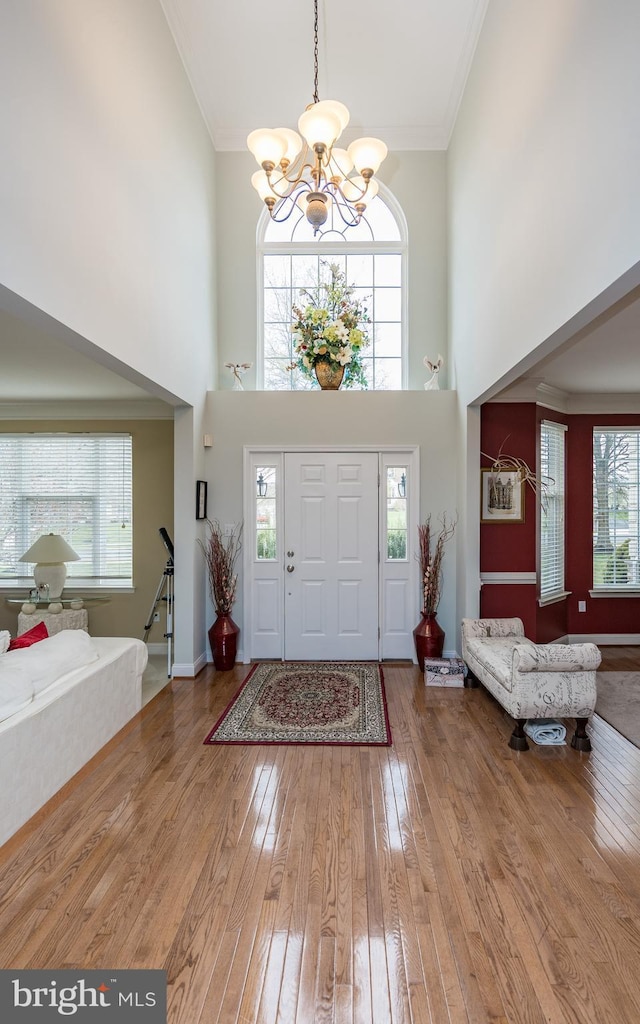 foyer entrance featuring a chandelier, wood-type flooring, a towering ceiling, and ornamental molding