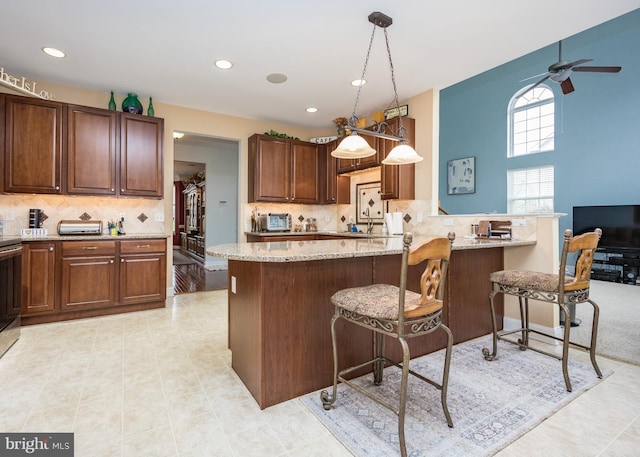 kitchen with decorative backsplash, a ceiling fan, a kitchen bar, and light stone countertops