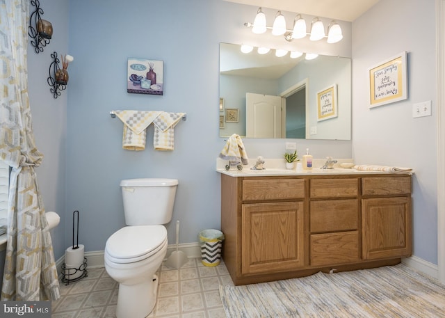 bathroom with a sink, baseboards, double vanity, and toilet