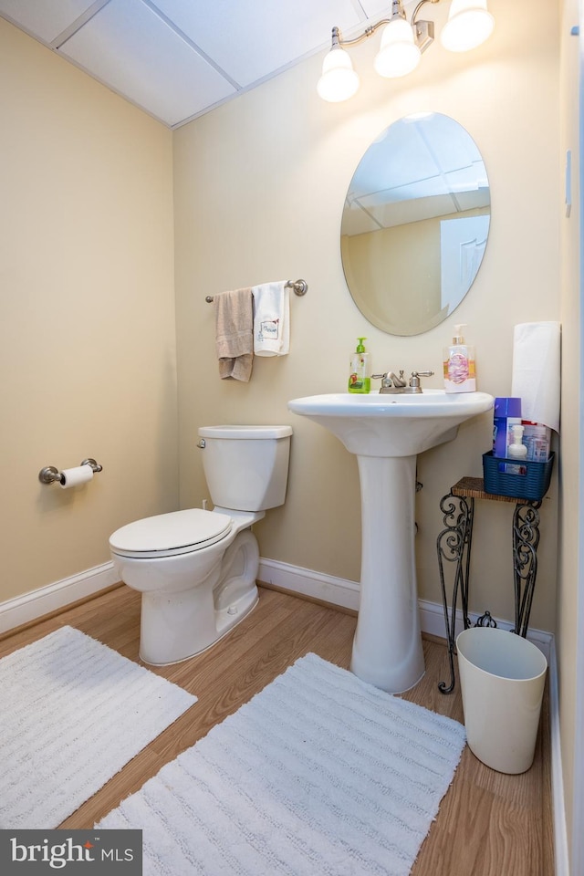 half bathroom with a sink, toilet, wood finished floors, and baseboards