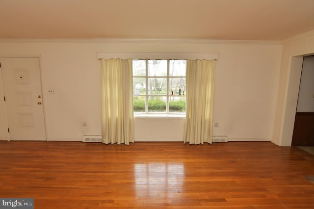 spare room featuring baseboard heating, crown molding, wood finished floors, and visible vents