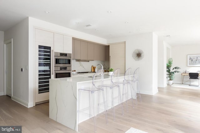 kitchen featuring light wood-style floors, stainless steel double oven, wine cooler, modern cabinets, and light stone countertops