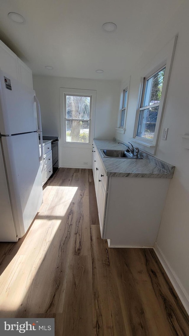 kitchen featuring light wood-type flooring, freestanding refrigerator, a sink, and white cabinets