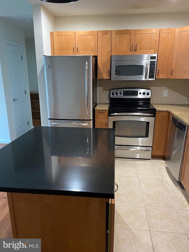 kitchen featuring dark stone countertops, light tile patterned floors, stainless steel appliances, backsplash, and a kitchen island