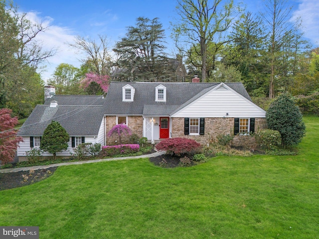 cape cod-style house featuring a chimney, roof with shingles, a front yard, and stone siding