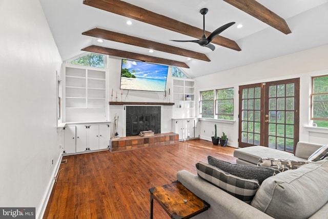living area with a tiled fireplace, lofted ceiling with beams, wood finished floors, a ceiling fan, and french doors