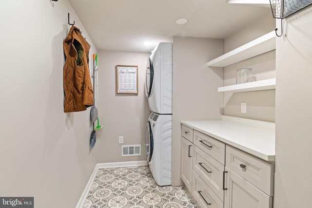 washroom featuring cabinet space, stacked washer / drying machine, visible vents, and baseboards