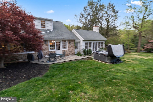 back of property featuring a patio area, a hot tub, a lawn, stone siding, and a chimney