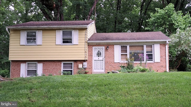 tri-level home featuring brick siding, a front yard, and a shingled roof