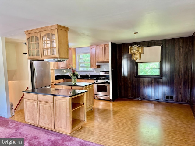 kitchen with appliances with stainless steel finishes, dark countertops, a chandelier, light wood-type flooring, and wood walls