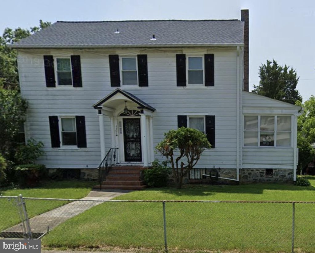 colonial home featuring a front yard, a shingled roof, fence, and a chimney