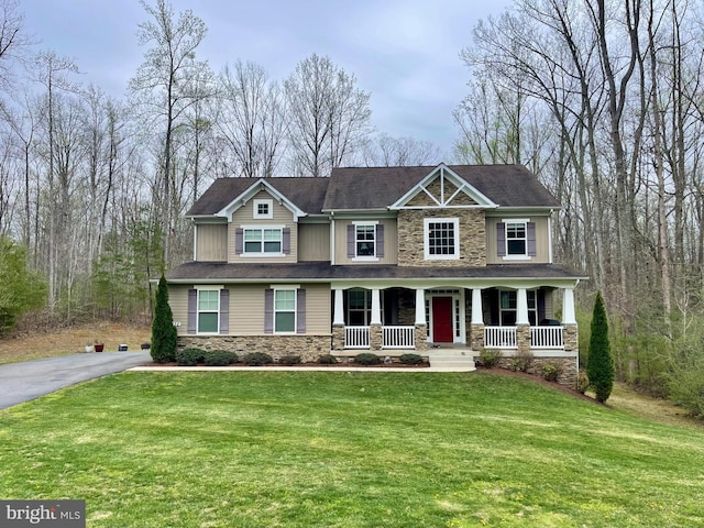 craftsman inspired home with a front yard, driveway, stone siding, and covered porch
