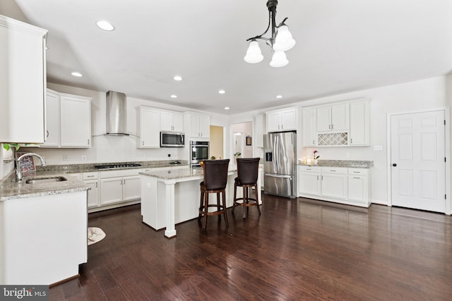 kitchen with recessed lighting, appliances with stainless steel finishes, wall chimney range hood, a sink, and a notable chandelier