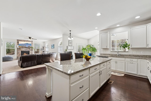 kitchen with light stone counters, white cabinets, a sink, a kitchen island, and a stone fireplace