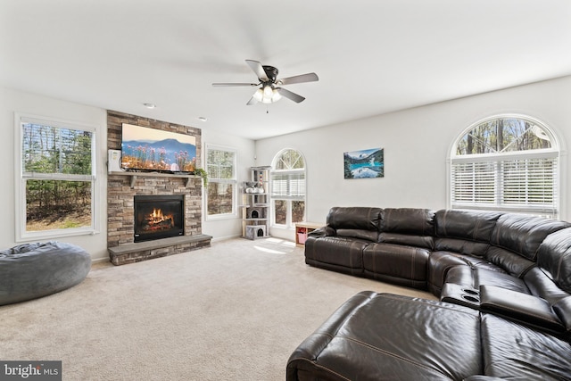 living area with a ceiling fan, a stone fireplace, and carpet floors