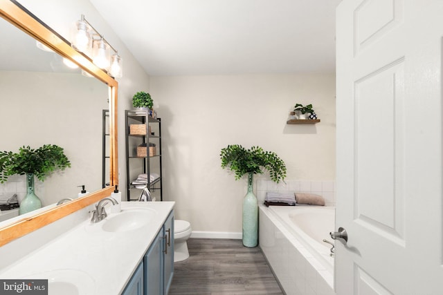 bathroom featuring a sink, toilet, double vanity, wood finished floors, and a garden tub