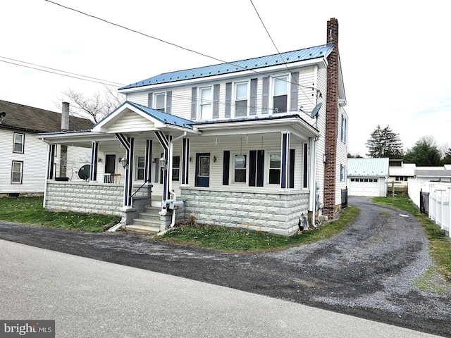 view of front facade with a chimney, an outbuilding, a garage, metal roof, and a porch