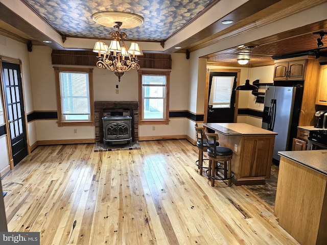 kitchen featuring light wood-style floors, a tray ceiling, a wood stove, and stainless steel fridge